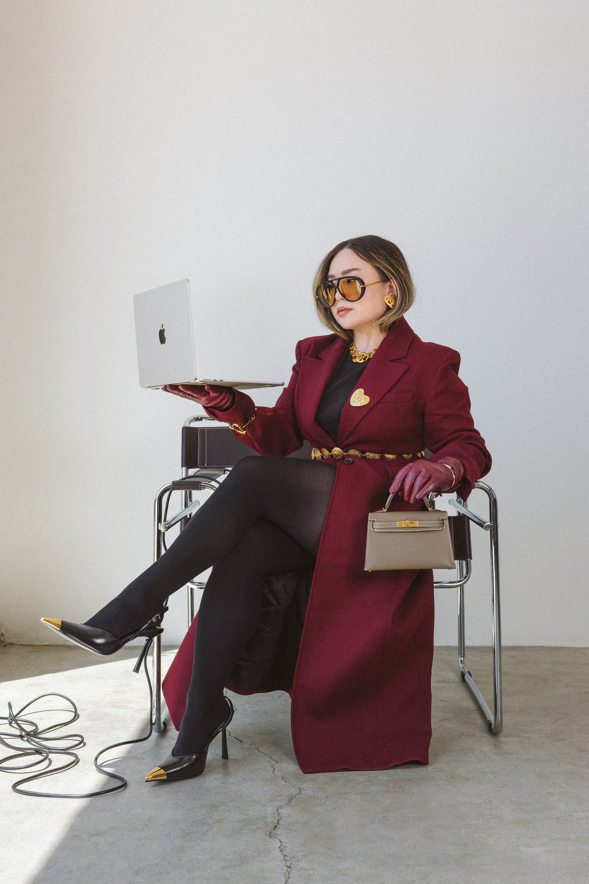 Woman in a long red coat holding a laptop, sitting on a chair with a white background