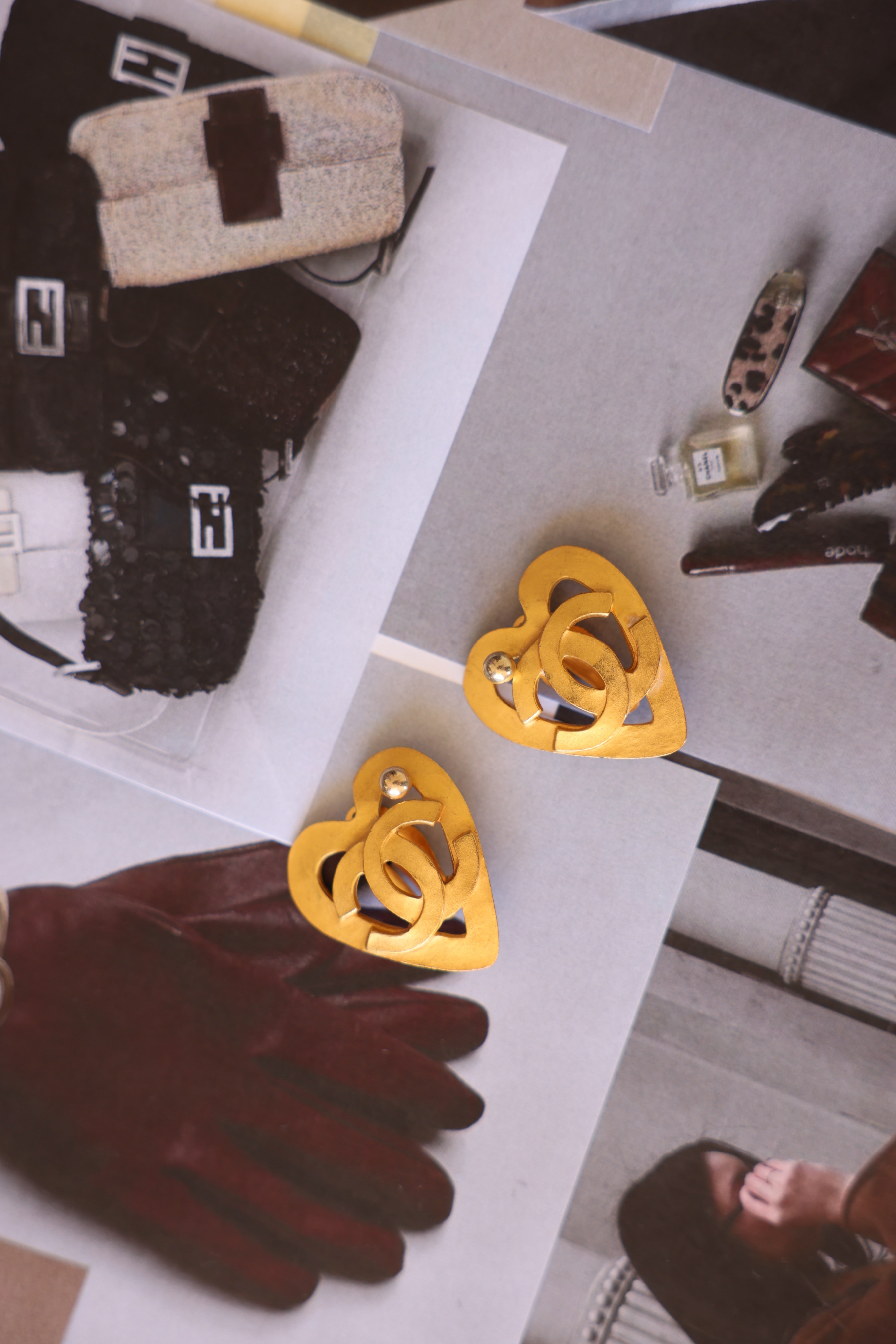 Yellow heart-shaped earrings displayed on a magazine with a hand wearing a glove and other items in the background.
