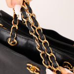 Black handbag with gold chain handle held by a hand against a white background