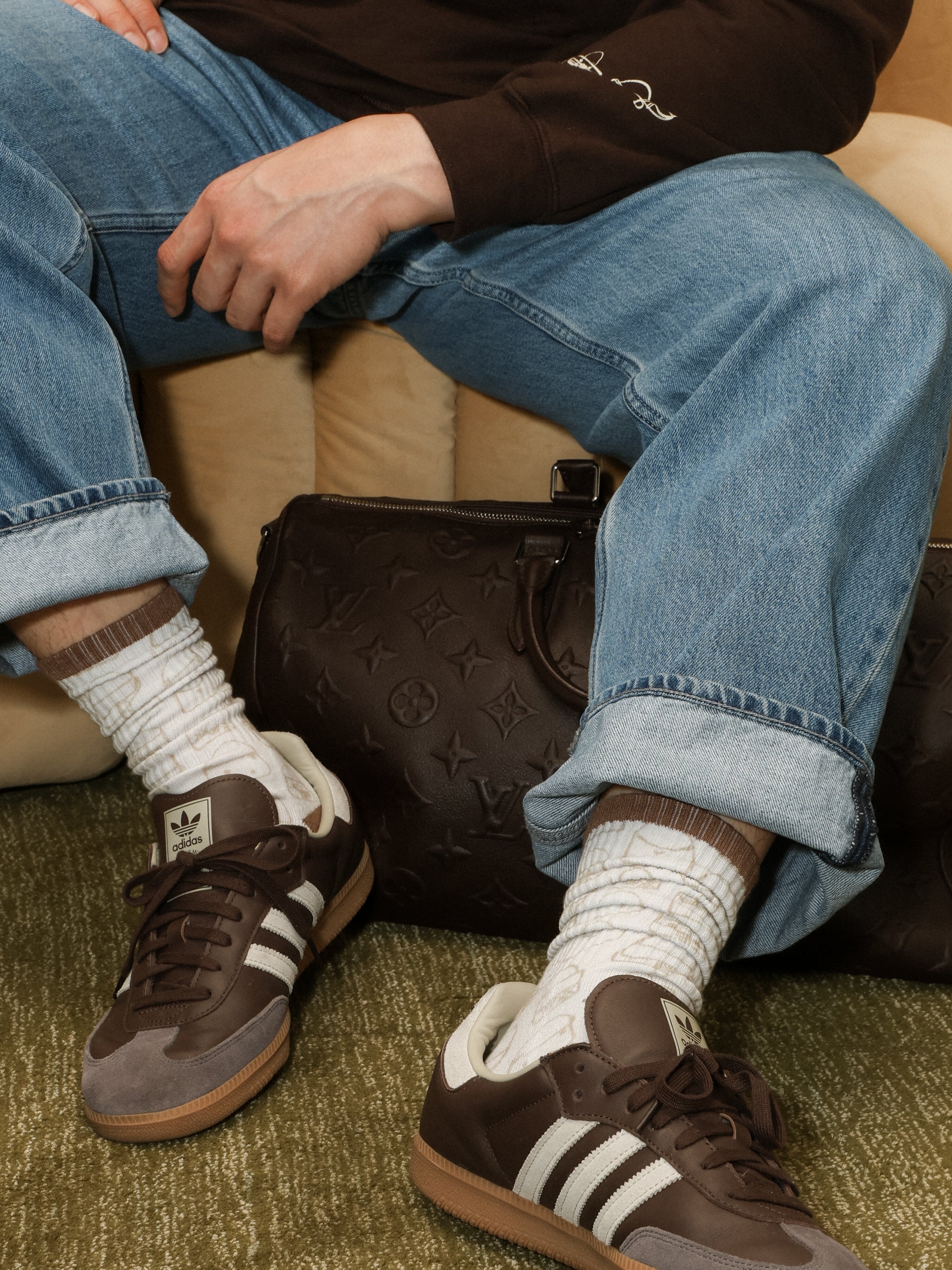 Person wearing brown sneakers with white stripes, blue jeans, and white socks sitting on a couch.