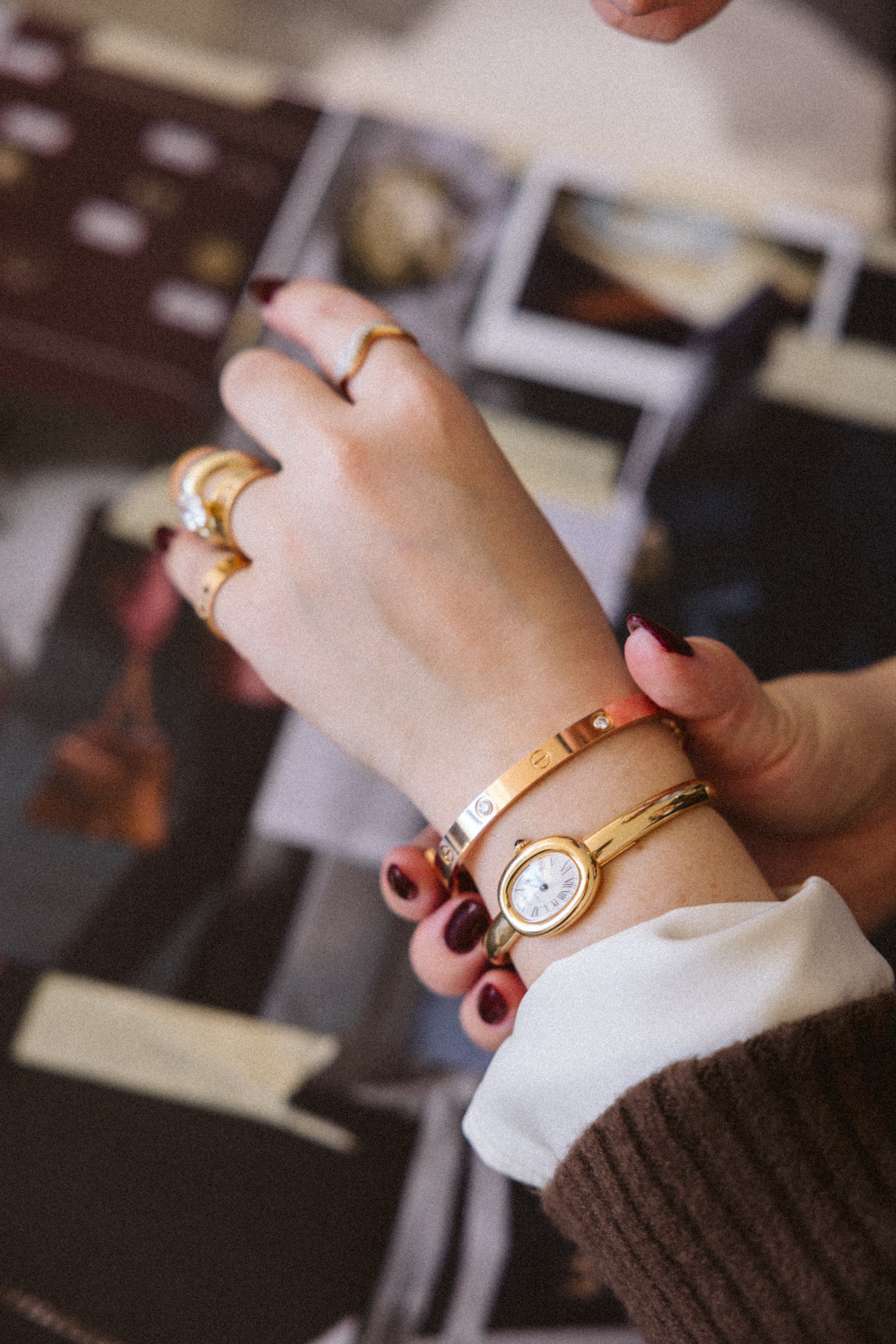 Close-up of a hand wearing multiple gold rings and a watch, with a blurred background.