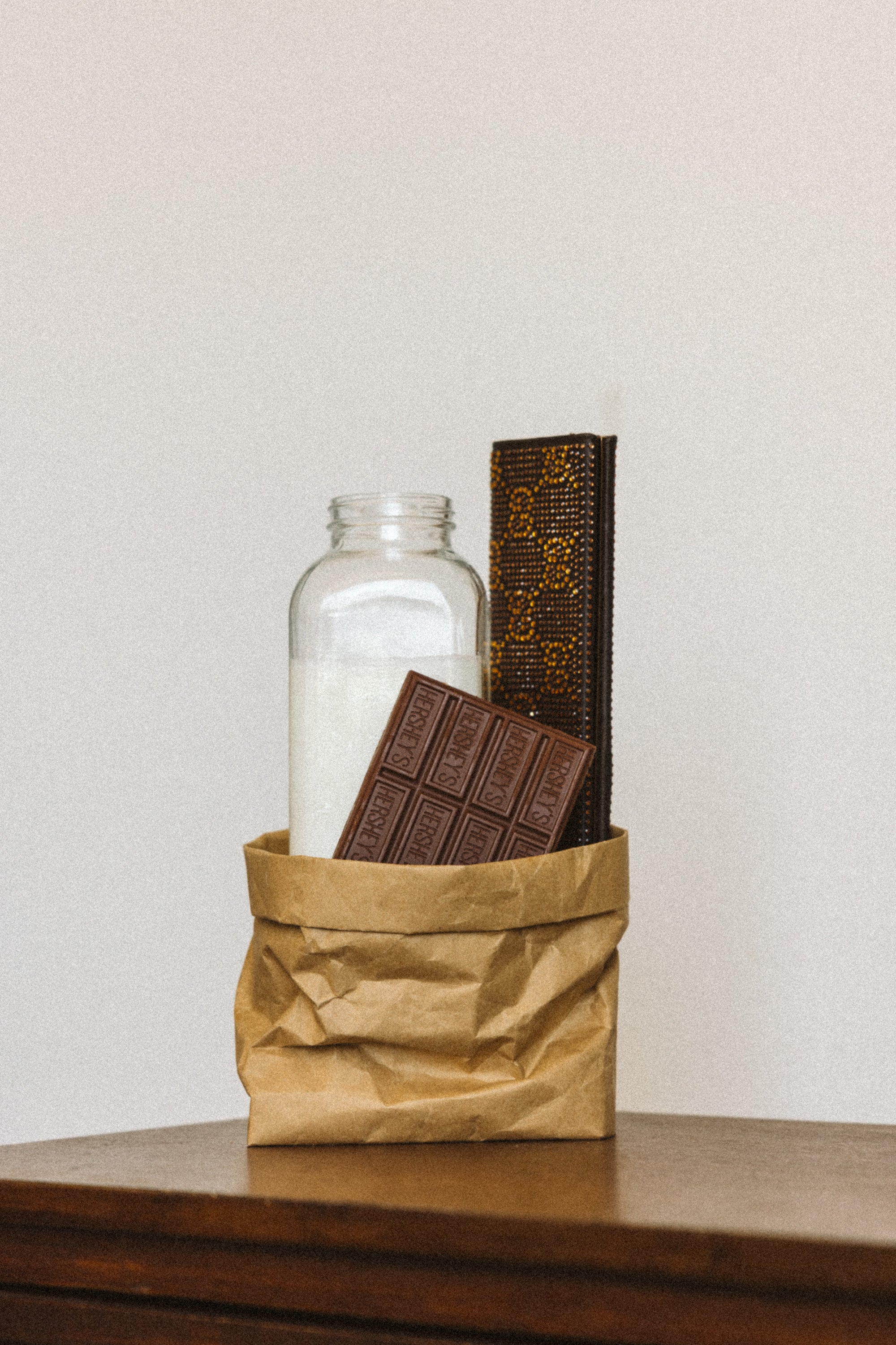 Glass jar with a bar of chocolate and a book on a wooden surface.