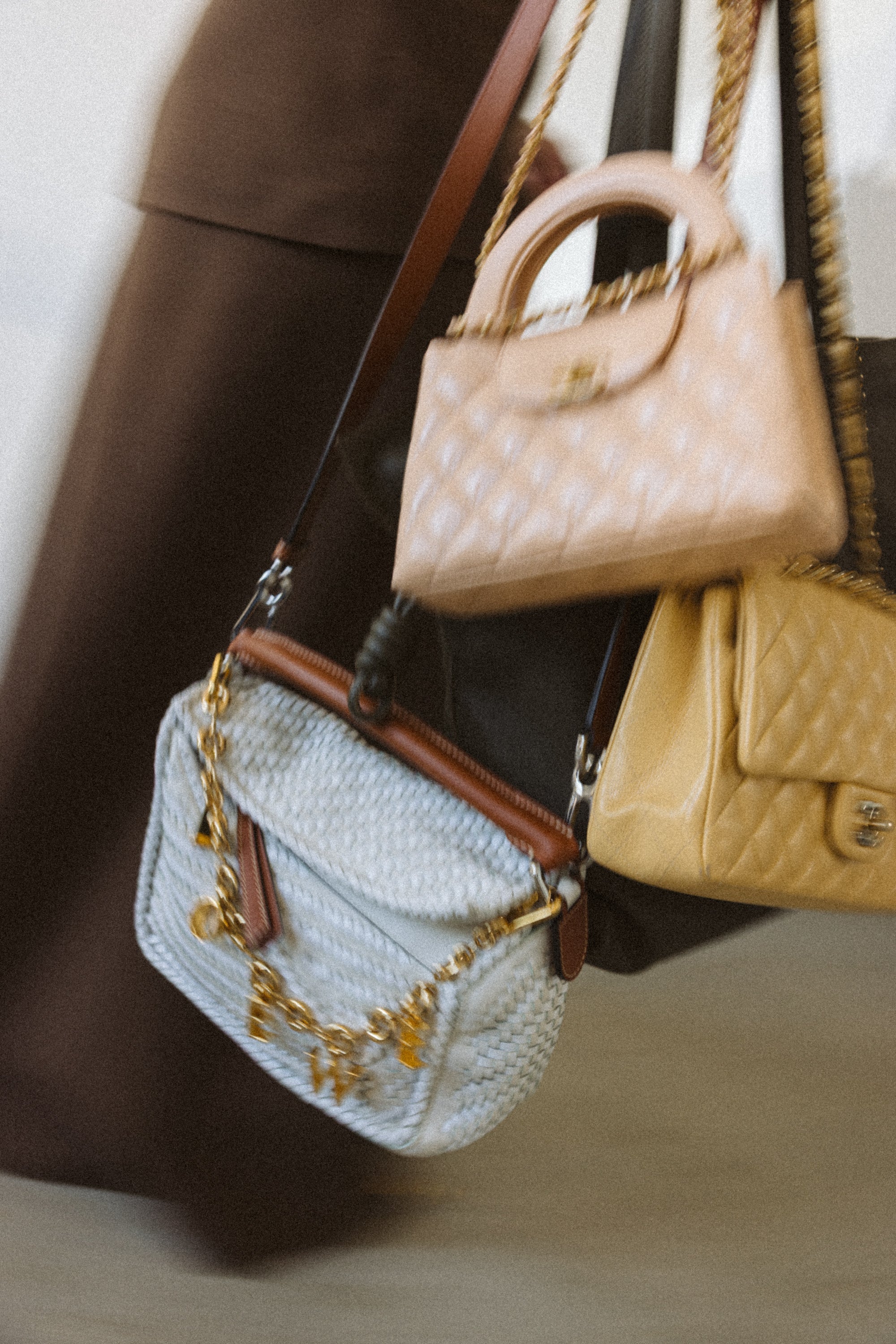 Three handbags of different colors held by a person wearing a brown coat.